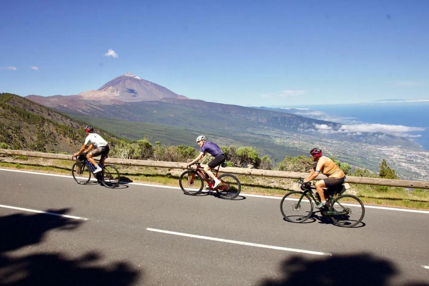 Tres ciclistas en carretera con el Teide y el mar al fondo