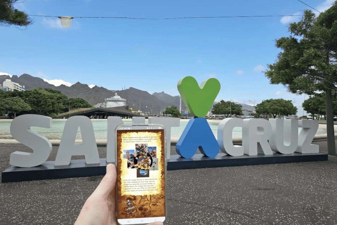 Móvil con la app del juego delante del cartel de Santa Cruz