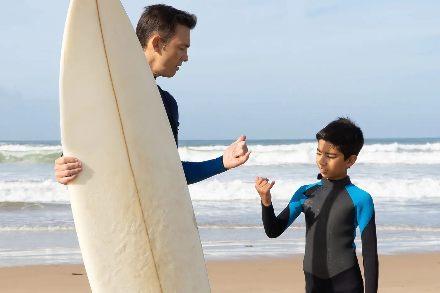 Surflehrer erklärt einem Schüler am Strand, bevor es ins Wasser geht